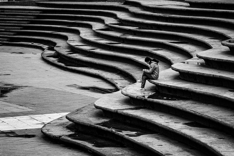 A lone figure sitting on curved, geometric steps in Istanbul, captured in black and white.