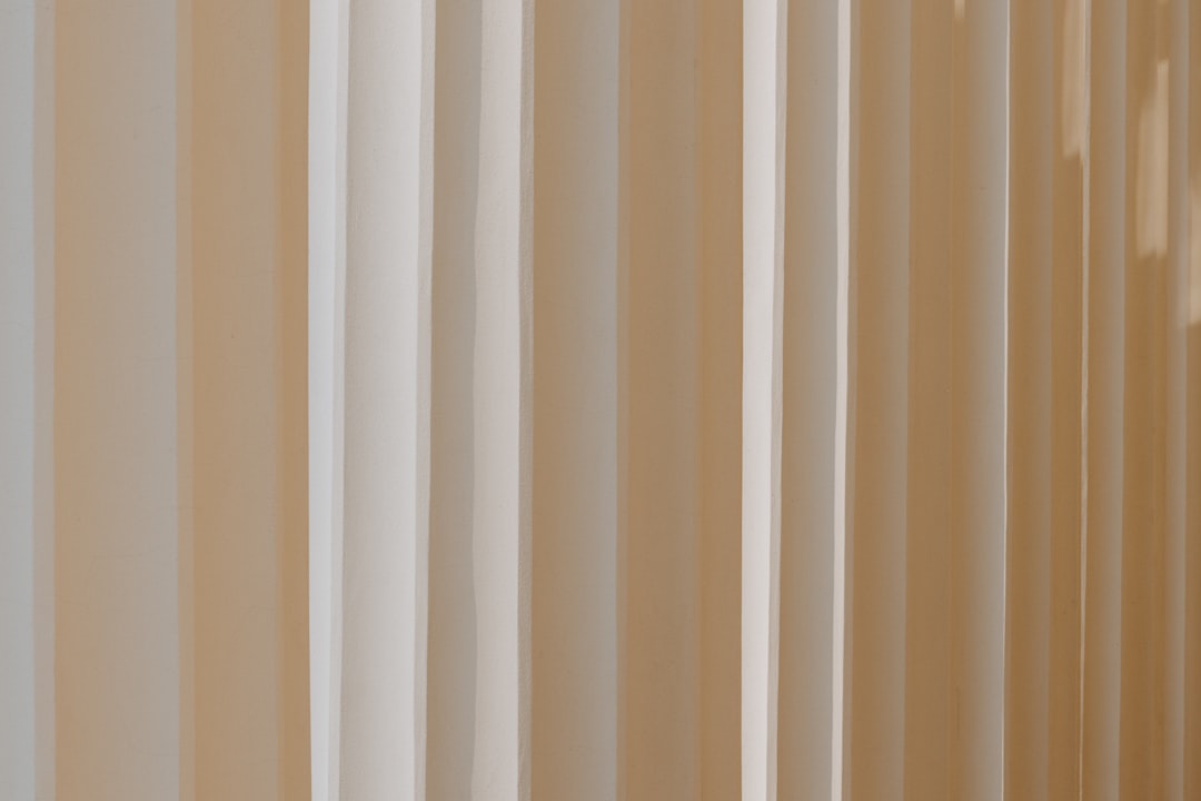 Vertical beige and white stripes with soft shadows on a textured surface.